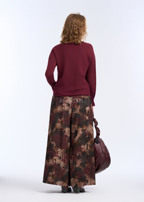 Modelka w bordowej, gładkiej bluzce z długim rękawem i prostym dekoltem; luźny fason, miękka dzianina, bluzka zestawiona z długim naszyjnikiem w kolorze złota