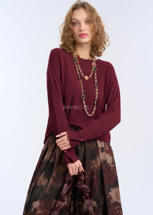 Modelka w bordowej, gładkiej bluzce z długim rękawem i prostym dekoltem; luźny fason, miękka dzianina, bluzka zestawiona z długim naszyjnikiem w kolorze złota