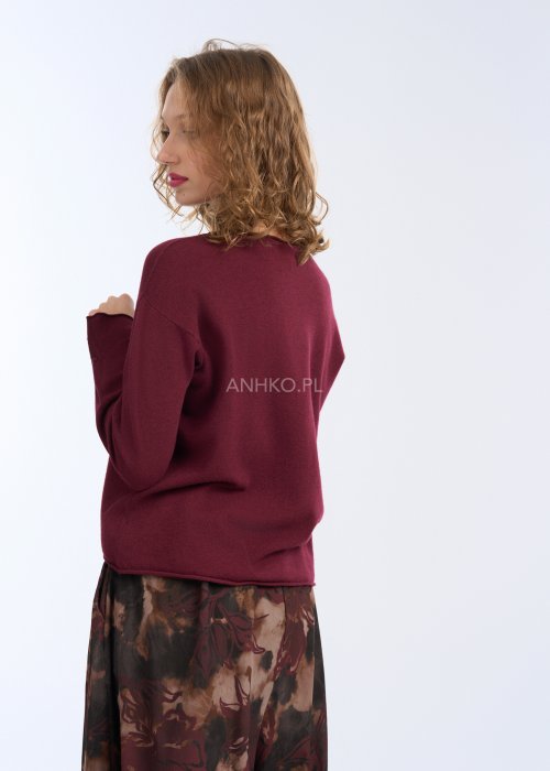 Modelka w bordowej, gładkiej bluzce z długim rękawem i prostym dekoltem; luźny fason, miękka dzianina, bluzka zestawiona z długim naszyjnikiem w kolorze złota