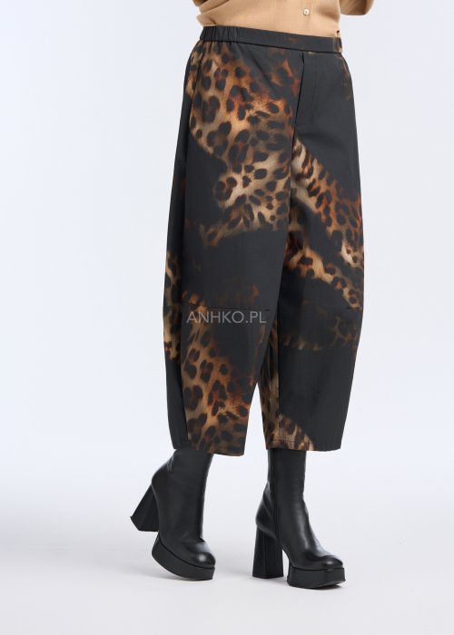 Szerokie spodnie damskie o długości 7/8, czarne z wyraźnym brązowym wzorem zwierzęcym (panterka), proste nogawki, gładki pas w talii; zestawione z czarnymi botkami na platformie