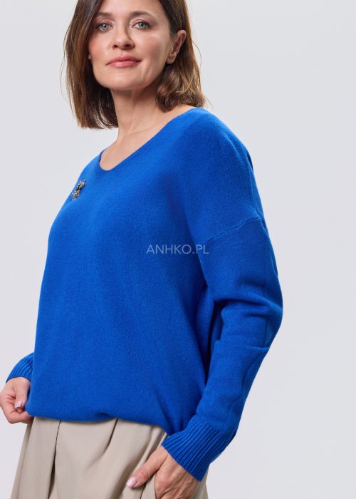 Kobaltowy sweter damski z miękkiej dzianiny, zintegrowany z długim szalem luźno opadającym przy dekolcie; model o swobodnym kroju, długi rękaw, stylizowany na jasnym tle