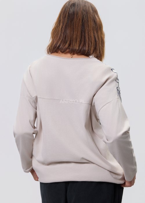 Jasna bluzka damska z długim rękawem, wykonana z lekkiej tkaniny, z dekoracyjnym haftem w kontrastowy kwiatowy wzór na przodzie; prosty, swobodny krój, okrągły dekolt, stylizacja na jasnym tle