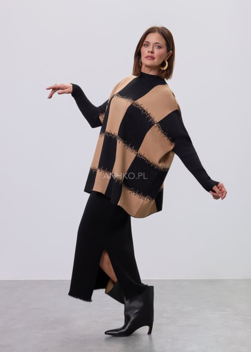 Beżowo-czarna damska tunika z dzianiny o luźnym kroju, z geometrycznym wzorem pasów i półgolfem, długie rękawy, prezentowana na modelce na jasnym tle
