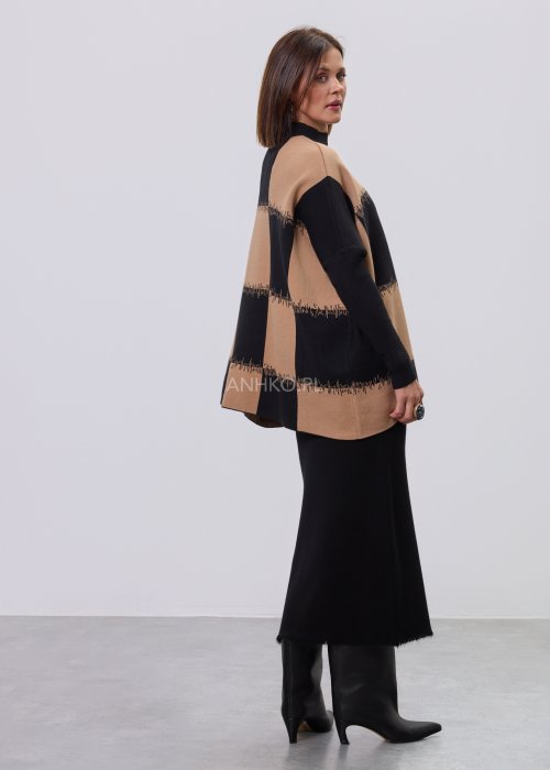 Beżowo-czarna damska tunika z dzianiny o luźnym kroju, z geometrycznym wzorem pasów i półgolfem, długie rękawy, prezentowana na modelce na jasnym tle