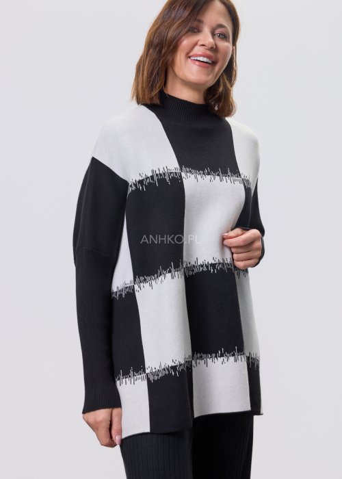 Czarno-biała damska tunika dzianinowa o luźnym kroju, z półgolfem i długimi rękawami, w geometryczny wzór pasów z delikatnym motywem graficznym, prezentowana na modelce na jasnym tle