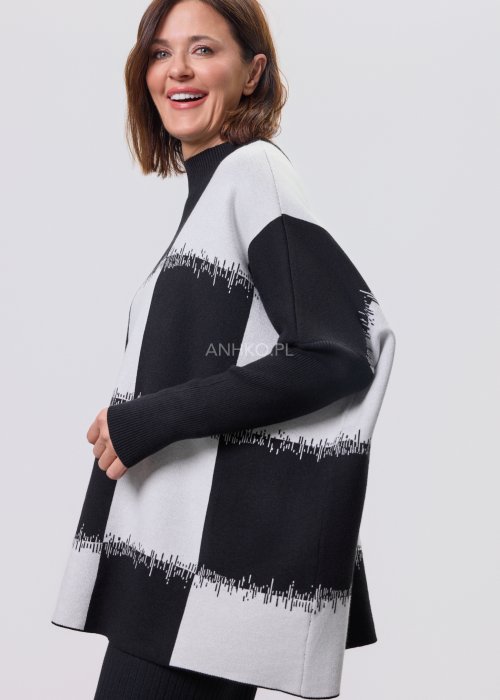 Czarno-biała damska tunika dzianinowa o luźnym kroju, z półgolfem i długimi rękawami, w geometryczny wzór pasów z delikatnym motywem graficznym, prezentowana na modelce na jasnym tle