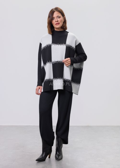Czarno-biała damska tunika dzianinowa o luźnym kroju, z półgolfem i długimi rękawami, w geometryczny wzór pasów z delikatnym motywem graficznym, prezentowana na modelce na jasnym tle