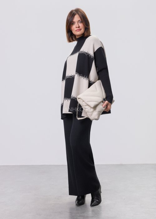 Czarno-ecru damska tunika dzianinowa o luźnym kroju, z półgolfem i długimi rękawami, w geometryczny wzór pasów z delikatnym motywem graficznym, prezentowana na modelce na jasnym tle