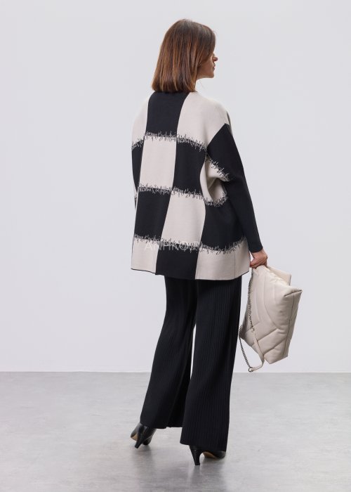 Czarno-ecru damska tunika dzianinowa o luźnym kroju, z półgolfem i długimi rękawami, w geometryczny wzór pasów z delikatnym motywem graficznym, prezentowana na modelce na jasnym tle