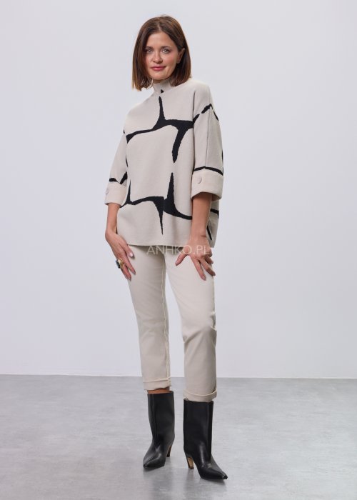 Ecru damski sweter o luźnym kroju z półgolfem i rękawami 3/4, zdobiony kontrastowym białym, abstrakcyjnym wzorem, prezentowany na modelce na jasnym tle