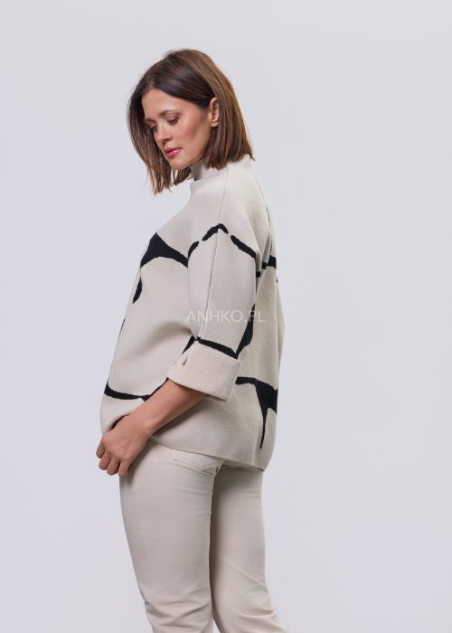 Ecru damski sweter o luźnym kroju z półgolfem i rękawami 3/4, zdobiony kontrastowym białym, abstrakcyjnym wzorem, prezentowany na modelce na jasnym tle