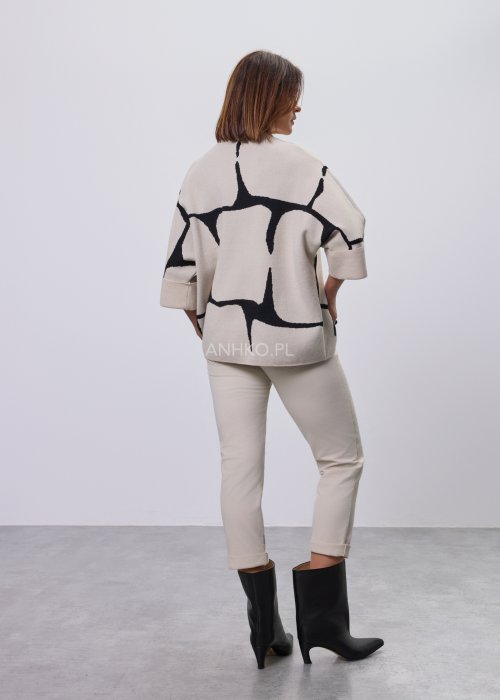 Ecru damski sweter o luźnym kroju z półgolfem i rękawami 3/4, zdobiony kontrastowym białym, abstrakcyjnym wzorem, prezentowany na modelce na jasnym tle