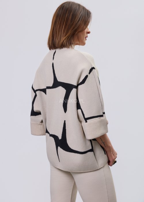 Ecru damski sweter o luźnym kroju z półgolfem i rękawami 3/4, zdobiony kontrastowym białym, abstrakcyjnym wzorem, prezentowany na modelce na jasnym tle