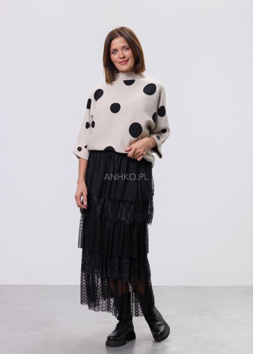 Jasny, beżowy damski sweter o luźnym kroju z półgolfem i rękawami 3/4, ozdobiony kontrastowym wzorem czarnych kropek, prezentowany na modelce na jasnym tle