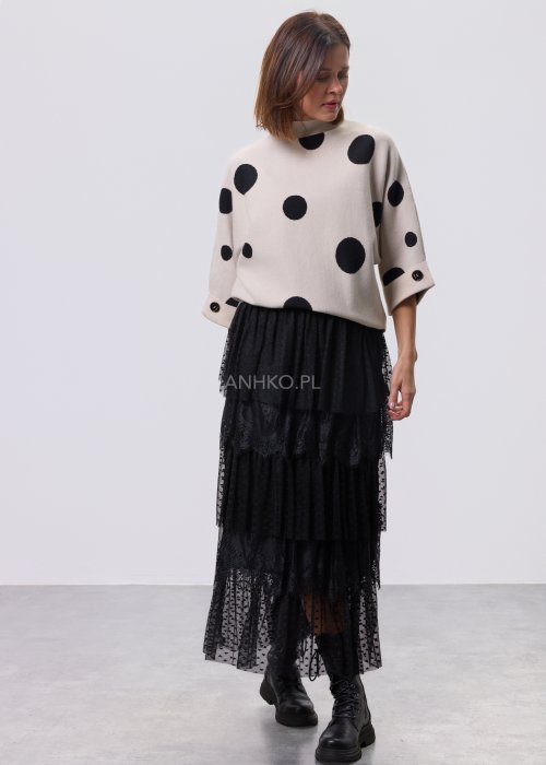Jasny, beżowy damski sweter o luźnym kroju z półgolfem i rękawami 3/4, ozdobiony kontrastowym wzorem czarnych kropek, prezentowany na modelce na jasnym tle