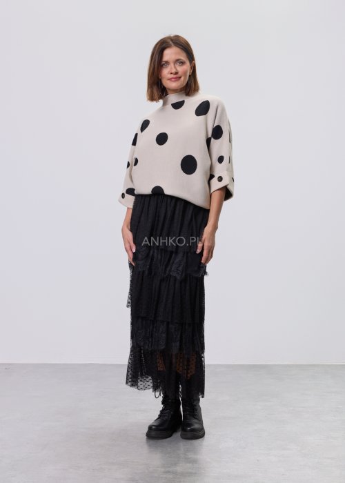 Jasny, beżowy damski sweter o luźnym kroju z półgolfem i rękawami 3/4, ozdobiony kontrastowym wzorem czarnych kropek, prezentowany na modelce na jasnym tle