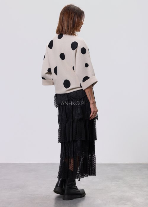 Jasny, beżowy damski sweter o luźnym kroju z półgolfem i rękawami 3/4, ozdobiony kontrastowym wzorem czarnych kropek, prezentowany na modelce na jasnym tle