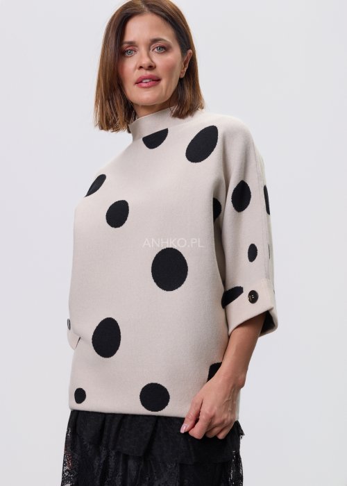 Jasny, beżowy damski sweter o luźnym kroju z półgolfem i rękawami 3/4, ozdobiony kontrastowym wzorem czarnych kropek, prezentowany na modelce na jasnym tle