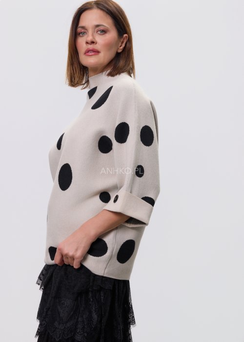 Jasny, beżowy damski sweter o luźnym kroju z półgolfem i rękawami 3/4, ozdobiony kontrastowym wzorem czarnych kropek, prezentowany na modelce na jasnym tle