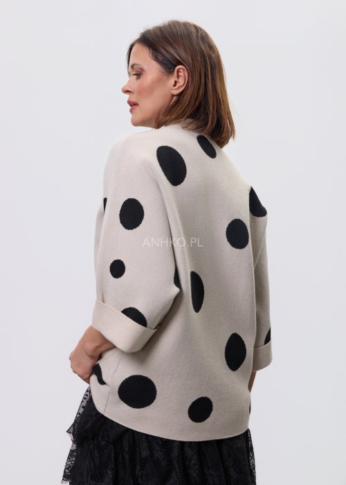 Jasny, beżowy damski sweter o luźnym kroju z półgolfem i rękawami 3/4, ozdobiony kontrastowym wzorem czarnych kropek, prezentowany na modelce na jasnym tle