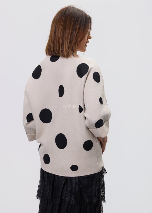 Jasny, beżowy damski sweter o luźnym kroju z półgolfem i rękawami 3/4, ozdobiony kontrastowym wzorem czarnych kropek, prezentowany na modelce na jasnym tle