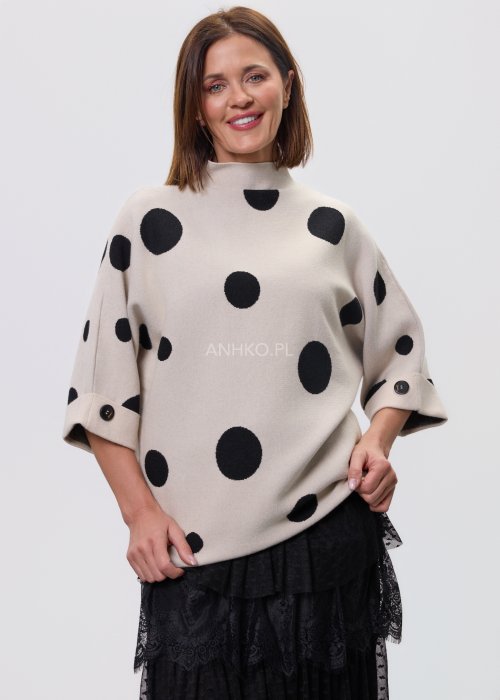 Jasny, beżowy damski sweter o luźnym kroju z półgolfem i rękawami 3/4, ozdobiony kontrastowym wzorem czarnych kropek, prezentowany na modelce na jasnym tle
