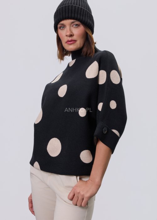 Czarny damski sweter o luźnym kroju z półgolfem i rękawami 3/4, ozdobiony kontrastowym wzorem beżowych kropek, prezentowany na modelce na jasnym tle