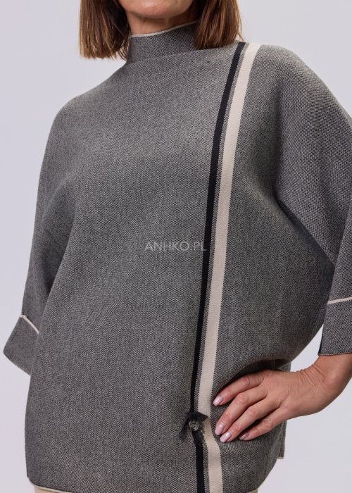 Damska, luźna bluzka o kroju oversize w kolorze szarym, z półgolfem i rękawami 3/4, ozdobiona pionowym kontrastowym paskiem, prezentowana na modelce na jasnym tle