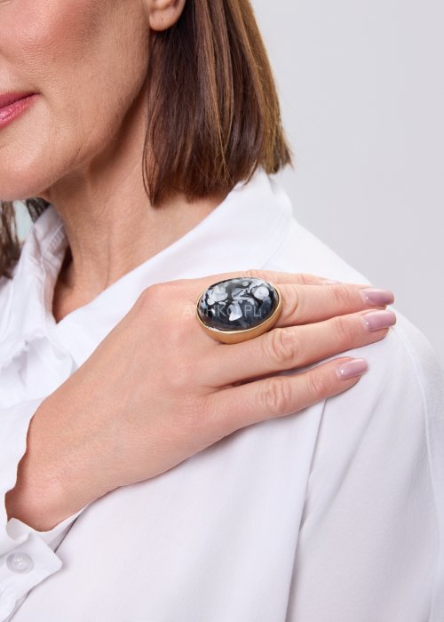 Duży pierścionek statement z czarnym kamieniem o marmurkowym wzorze w złotej oprawie, nowoczesna biżuteria damska noszona do białej koszuli, minimalistyczny styl