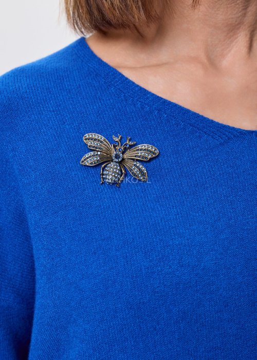 Złota broszka w kształcie pszczoły z granatowymi kryształkami przypięta do niebieskiego swetra, elegancki dodatek biżuteryjny do stylizacji damskiej