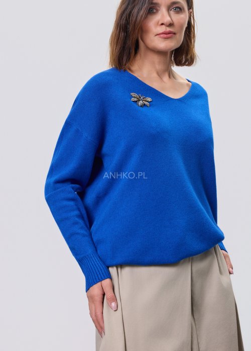 Złota broszka w kształcie pszczoły z granatowymi kryształkami przypięta do niebieskiego swetra, elegancki dodatek biżuteryjny do stylizacji damskiej
