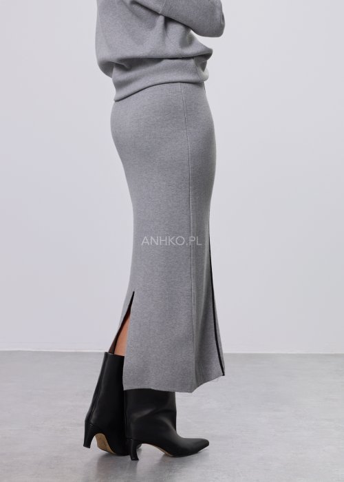 Modelka w szarym, dzianinowym komplecie dwuczęściowym: luźny sweter z długim rękawem i czarnym abstrakcyjnym nadrukiem z przodu oraz dopasowana spódnica midi w tym samym kolorze