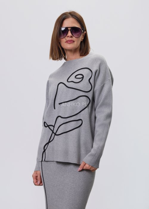 Modelka w szarym, dzianinowym komplecie dwuczęściowym: luźny sweter z długim rękawem i czarnym abstrakcyjnym nadrukiem z przodu oraz dopasowana spódnica midi w tym samym kolorze