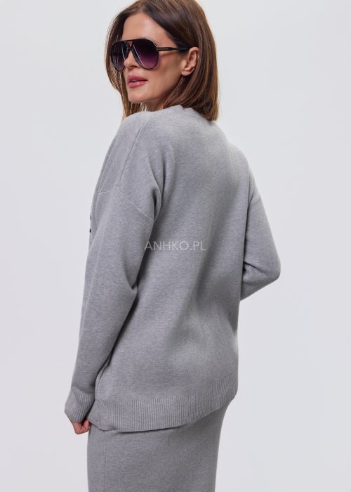 Modelka w szarym, dzianinowym komplecie dwuczęściowym: luźny sweter z długim rękawem i czarnym abstrakcyjnym nadrukiem z przodu oraz dopasowana spódnica midi w tym samym kolorze