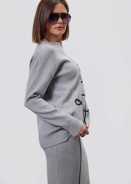 Modelka w szarym, dzianinowym komplecie dwuczęściowym: luźny sweter z długim rękawem i czarnym abstrakcyjnym nadrukiem z przodu oraz dopasowana spódnica midi w tym samym kolorze