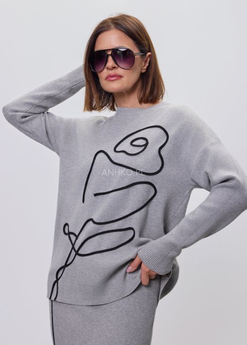 Modelka w szarym, dzianinowym komplecie dwuczęściowym: luźny sweter z długim rękawem i czarnym abstrakcyjnym nadrukiem z przodu oraz dopasowana spódnica midi w tym samym kolorze