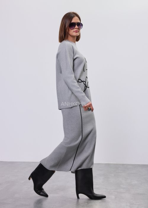 Modelka w szarym, dzianinowym komplecie dwuczęściowym: luźny sweter z długim rękawem i czarnym abstrakcyjnym nadrukiem z przodu oraz dopasowana spódnica midi w tym samym kolorze