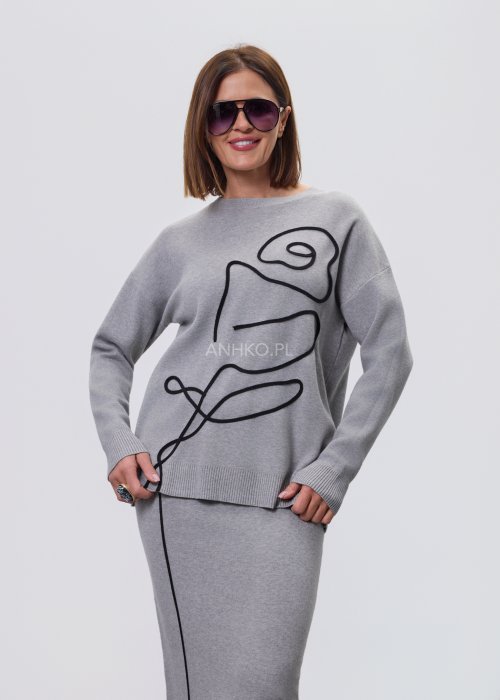 Modelka w szarym, dzianinowym komplecie dwuczęściowym: luźny sweter z długim rękawem i czarnym abstrakcyjnym nadrukiem z przodu oraz dopasowana spódnica midi w tym samym kolorze