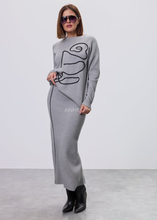 Modelka w szarym, dzianinowym komplecie dwuczęściowym: luźny sweter z długim rękawem i czarnym abstrakcyjnym nadrukiem z przodu oraz dopasowana spódnica midi w tym samym kolorze