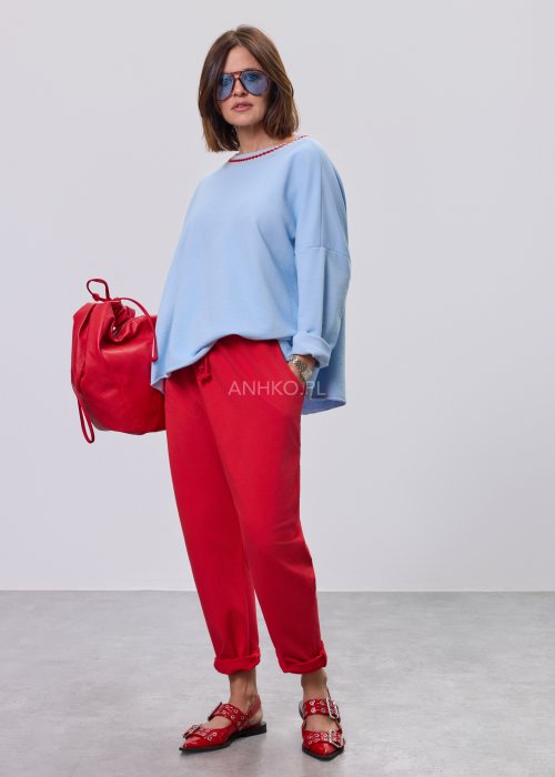 Niebieska bluza damska oversize w odcieniu baby blue z asymetrycznym dołem i kontrastowym dekoltem. Stylizacja z czerwonymi spodniami podkreśla nowoczesny charakter modelu.