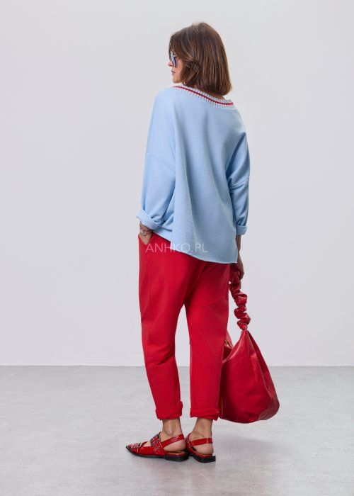Niebieska bluza damska oversize w odcieniu baby blue z asymetrycznym dołem i kontrastowym dekoltem. Stylizacja z czerwonymi spodniami podkreśla nowoczesny charakter modelu.