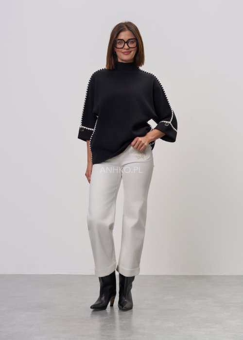 Czarna damska bluzka o luźnym kroju, z półgolfem i rękawami 3/4, ozdobiona kontrastową białą lamówką wzdłuż ramion i rękawów oraz dekoracyjnymi guzikami.