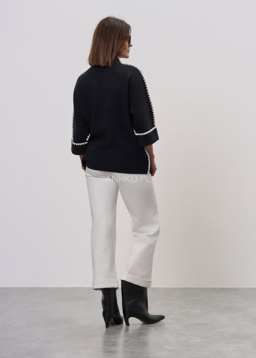 Czarna damska bluzka o luźnym kroju, z półgolfem i rękawami 3/4, ozdobiona kontrastową białą lamówką wzdłuż ramion i rękawów oraz dekoracyjnymi guzikami.