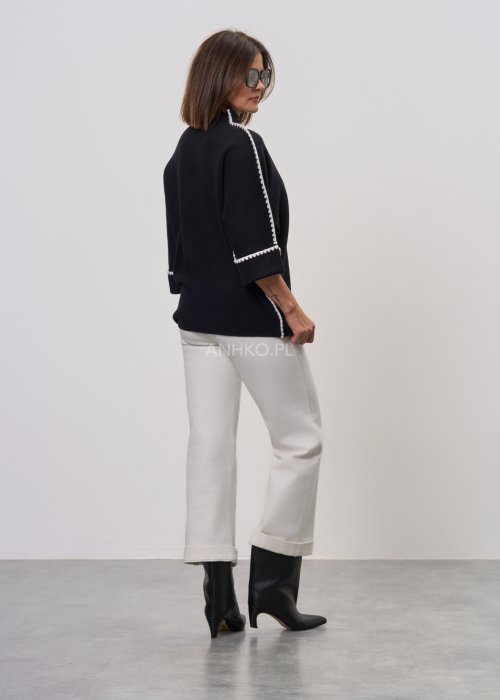 Czarna damska bluzka o luźnym kroju, z półgolfem i rękawami 3/4, ozdobiona kontrastową białą lamówką wzdłuż ramion i rękawów oraz dekoracyjnymi guzikami.