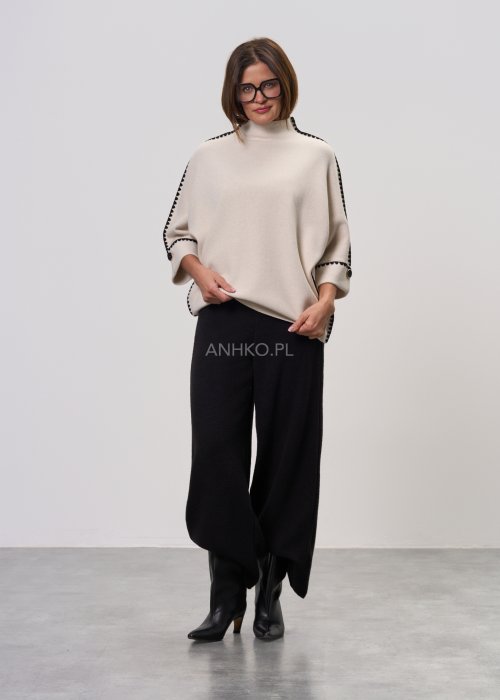 Beżowa damska bluzka o luźnym kroju, z półgolfem i rękawami 3/4, wykończona kontrastową czarną lamówką wzdłuż ramion, rękawów i boków oraz ozdobnymi guzikami przy mankietach.