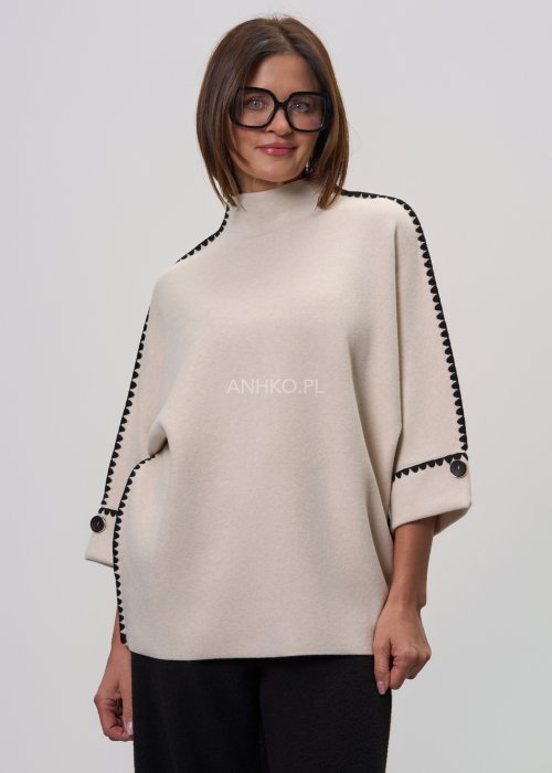 Beżowa damska bluzka o luźnym kroju, z półgolfem i rękawami 3/4, wykończona kontrastową czarną lamówką wzdłuż ramion, rękawów i boków oraz ozdobnymi guzikami przy mankietach.