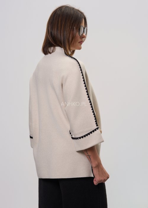 Beżowa damska bluzka o luźnym kroju, z półgolfem i rękawami 3/4, wykończona kontrastową czarną lamówką wzdłuż ramion, rękawów i boków oraz ozdobnymi guzikami przy mankietach.
