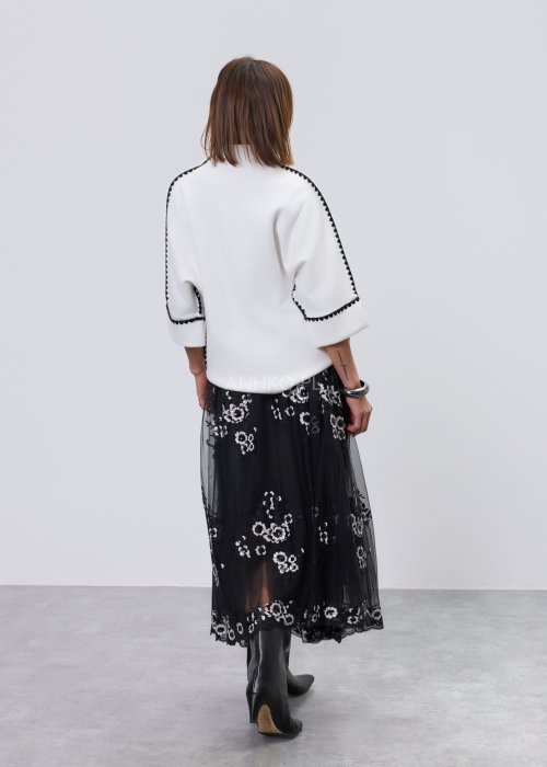 Biała damska bluzka o luźnym kroju z półgolfem i rękawami 3/4, wykończona kontrastową czarną lamówką wzdłuż ramion, rękawów i boków oraz ozdobnymi guzikami przy mankietach