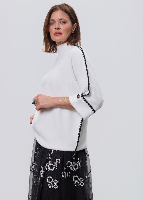 Biała damska bluzka o luźnym kroju z półgolfem i rękawami 3/4, wykończona kontrastową czarną lamówką wzdłuż ramion, rękawów i boków oraz ozdobnymi guzikami przy mankietach