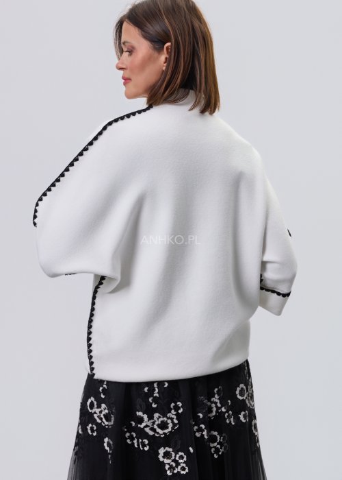 Biała damska bluzka o luźnym kroju z półgolfem i rękawami 3/4, wykończona kontrastową czarną lamówką wzdłuż ramion, rękawów i boków oraz ozdobnymi guzikami przy mankietach